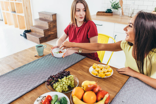 Mujeres amigas comiendo frutas y verduras en la cocina. Nutrición saludable. Comida baja en calorías
. - Foto, imagen