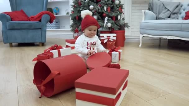 Adorable little kid in new year clothes with bobble hat playing with lid from the box,sitting on the background of the beautifully decorated christmas house-room - Filmmaterial, Video
