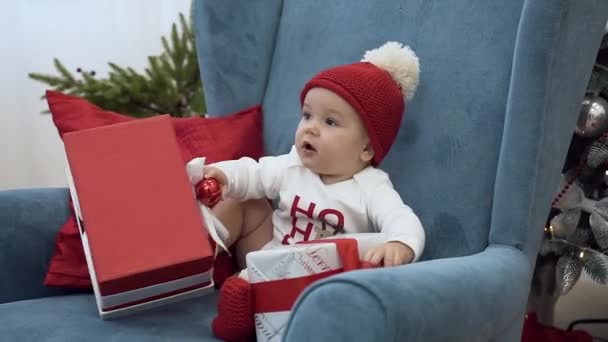 Wonderful toddler sitting in a big arm chair and playing with christmas presents - Metraje, vídeo