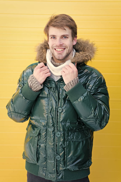 Guy wear warm jacket with hood. Feel comfortable in warm clothing. Keep warm. Comfortable winter clothing. Winter stylish menswear. Man bearded hipster wear warm jacket with fur yellow background - Photo, Image