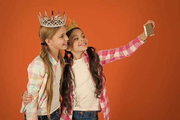 Kids wear golden crowns symbol princess. Warning signs of spoiled child. Avoid raising spoiled kids. Girls taking selfie photo smartphone camera. Spoiled children concept. Demand more attention - Fotó, kép