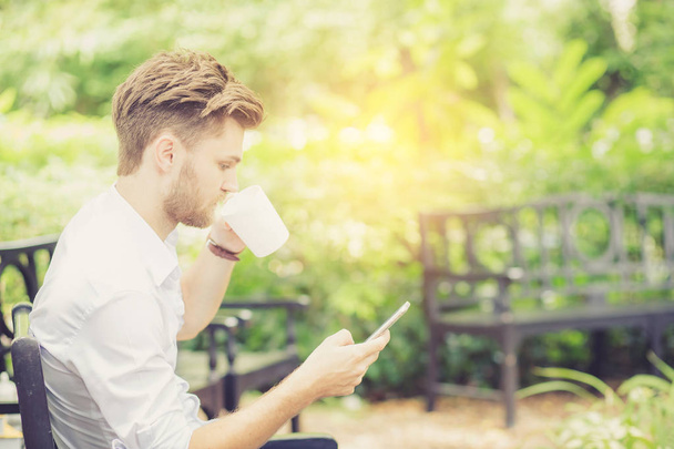 Бізнес молодий красивий чоловік п'є чашку кави за допомогою мобільного фені
 - Фото, зображення