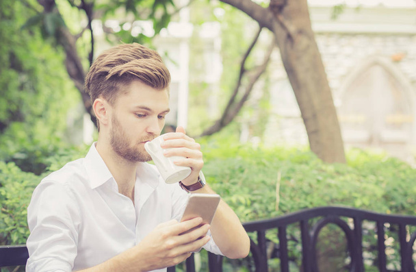Επιχείρηση νέος όμορφος άντρας πίνει φλιτζάνι καφέ χρησιμοποιώντας κινητό φο - Φωτογραφία, εικόνα