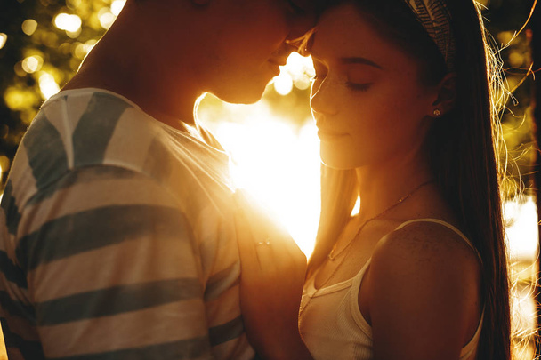 Primer plano de pareja joven con la cabeza tocando contra la puesta del sol
 - Foto, Imagen