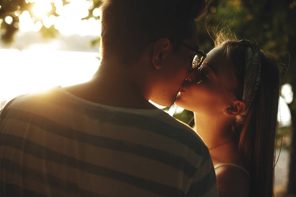 Close up portrait of a young cheerful couple kissing against sun - Fotoğraf, Görsel