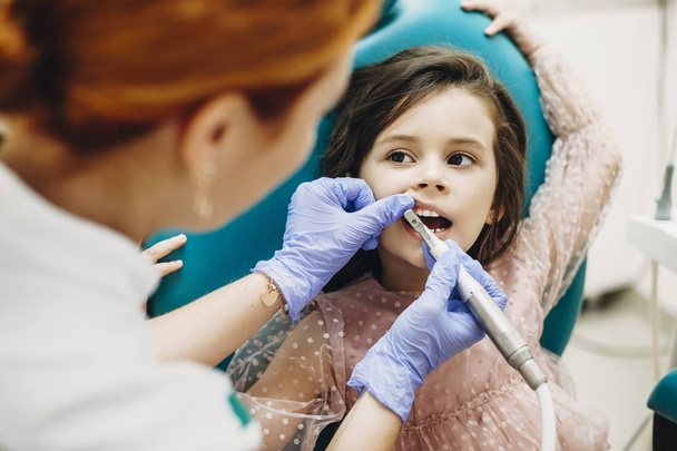 Carina bambina seduta su una sedia di stomatologia con un intervento chirurgico ai denti da un dentista pediatrico
. - Foto, immagini