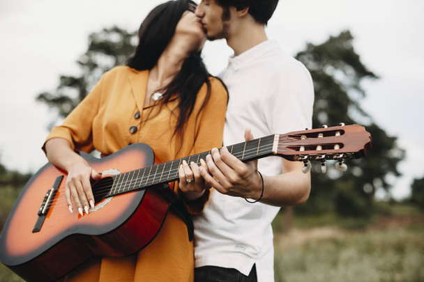 Hands of a young couple holding a guitar while kissing outside in nature. - Fotoğraf, Görsel