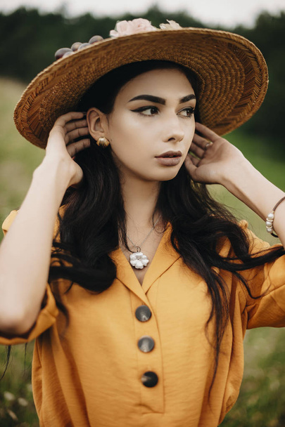 Close up portrait of a beautiful young woman looking away touching her hair outdoor. Lovely female with dark hair wearing hat. - Foto, Imagem