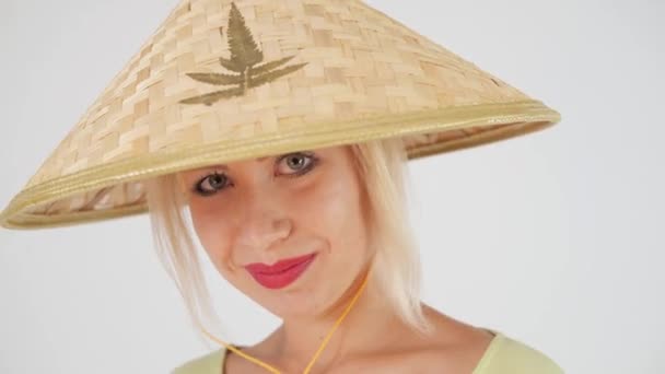 Close-up. Beautiful European girl on a white background in a straw conical hat (nonla), posing and smiling at the camera. - Záběry, video