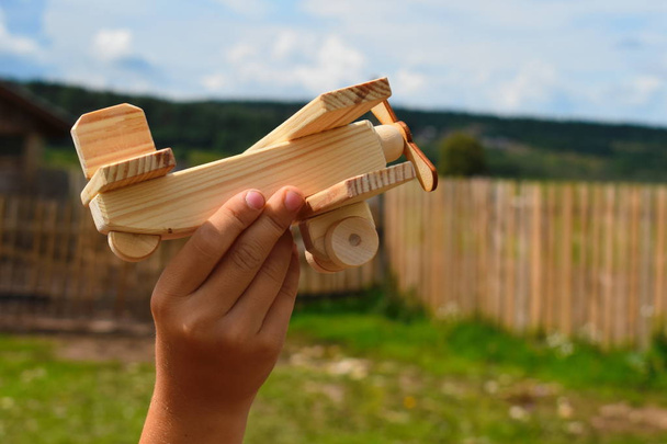 Boy plays with handmade wooden plane. Old rural retro toy plane on blue sky. Natural toy of last century.  - Fotó, kép