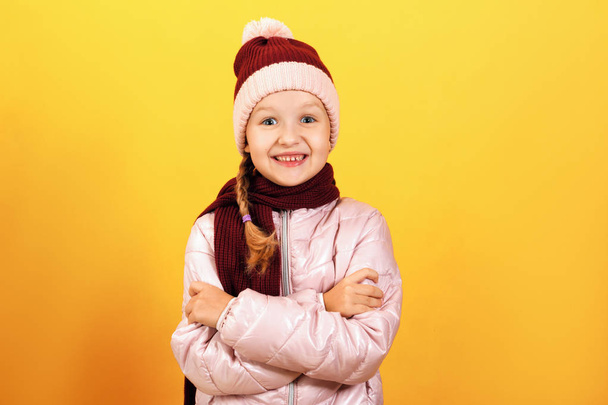 Autumn and winter concept. Portrait of a cute little girl in a jacket, scarf and hat on a yellow background - Fotoğraf, Görsel