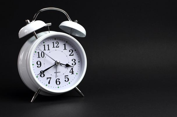 Clásico despertador blanco marcando reloj sobre fondo negro
 - Foto, Imagen