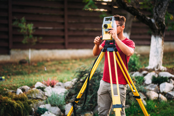 close up portrait of survey engineer using and working with total station theodolite at landscaping project - Fotó, kép
