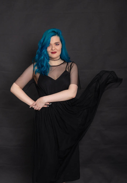 People and fashion concept - Woman dressed in black dress and blue hair posing over black background - Fotó, kép