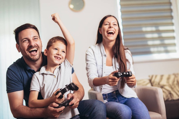 Lächelnde Familie sitzt zusammen auf der Couch und spielt Videospiele - Foto, Bild