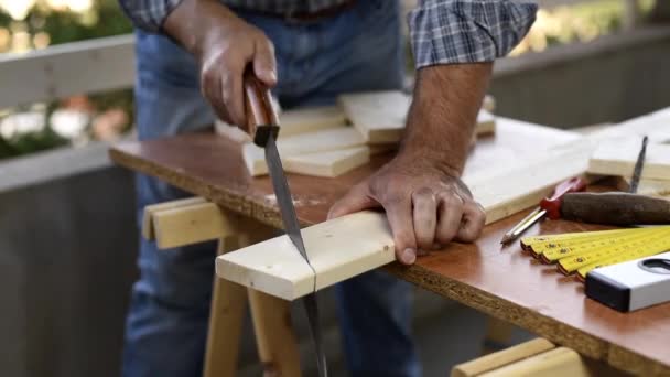 Adult craftsman carpenter with manual saw working on cutting a wooden table. Housework do it yourself. Footage. - Footage, Video