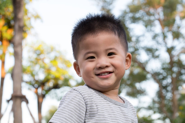Trochę Asian chłopak stojący i uśmiechnięty szczęśliwy na publiczny zielony ogród tło. Jeden rok pięć miesiąc stary - Zdjęcie, obraz