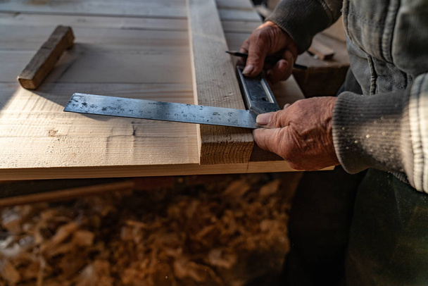 Cerca de la foto de las manos viejas del maestro carpintero que sostiene la regla y el lápiz, hace mediciones
 - Foto, imagen