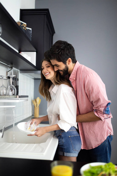 Young happy couple is washing dishes and hugging smiling - Photo, Image