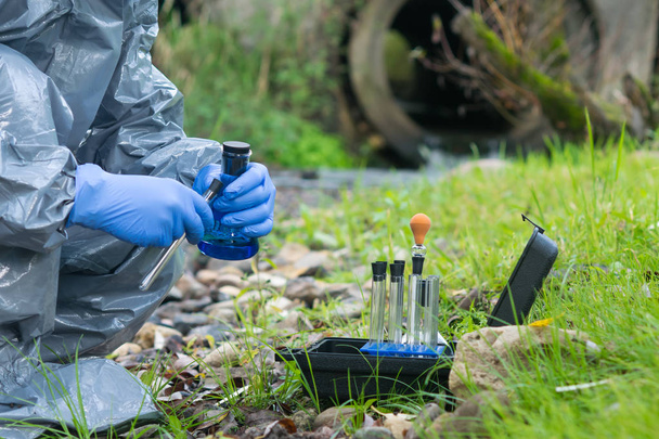 a worker in a protective suit takes samples of water and soil for contamination - Foto, Imagen