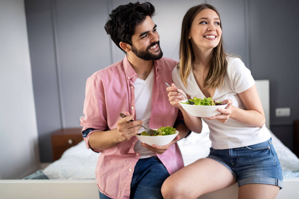 Beautiful young playful couple eating salad together - Foto, afbeelding