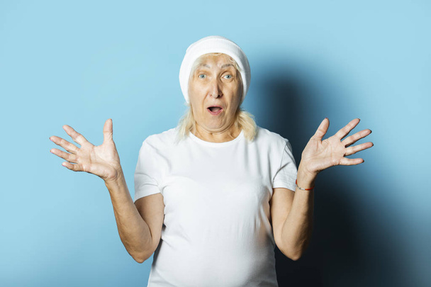 Mavi arka planda şapkalı komik yaşlı kadın. Modern tarzda havalı bir büyükanne kavramı. - Fotoğraf, Görsel