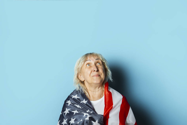 Oude vrouw houdt Amerikaanse vlag op een blauwe achtergrond. Independence Day viering concept, Memorial Day, emigratie, Amerikaanse vlag - Foto, afbeelding