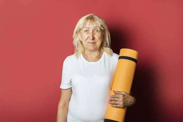 Vecchia donna tiene un tappetino karemat o yoga su uno sfondo rosa. Concetto di ginnastica, fitness, yoga per anziani
 - Foto, immagini
