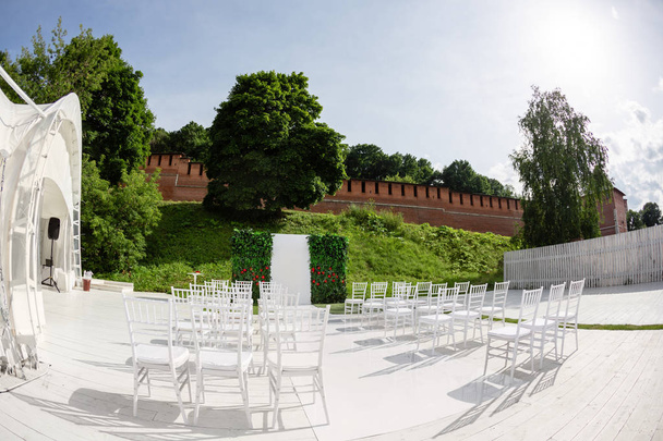 Rows of empty white chairs sitting on a wooden floor. Wedding chairs with flowers at ceremony outdoors - Photo, Image