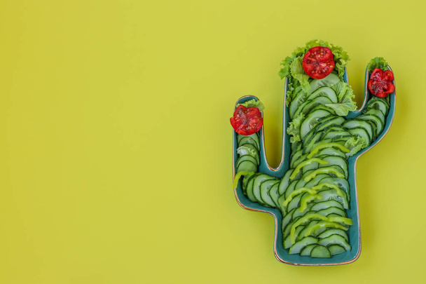 Green Cactus Shaped Dish with fresh salad of tomatoes, cucumbers, pepper and lettuce on yellow background: fiesta party, wild west party, copy space, horizontal orientation - Photo, Image