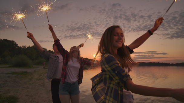 Allegro maschio e femmina amici stanno correndo lungo la spiaggia al tramonto, tenendo fuochi d'artificio scintillanti e luci in fuga al rallentatore. Festa danzante e al tramonto sulla spiaggia
. - Filmati, video