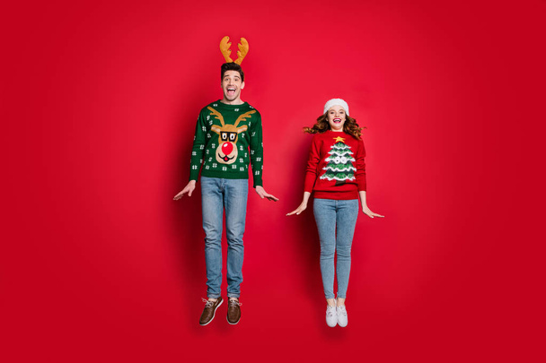 Full body photo of crazy lady and guy jumping high enjoy x-mas sale wear ugly ornament pullovers and headwear isolated red color background - Fotoğraf, Görsel