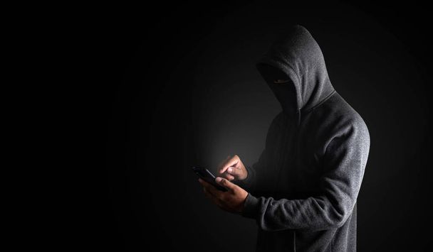 Hacker mit Smartphone. Männer in schwarzer Kleidung mit verstecktem Gesicht - Foto, Bild