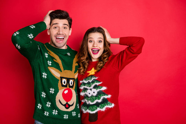 Portrait of impressed two hipster couple scream wow omg hear news wear reindeer christmas tree design decor funny sweater received by granny isolated over red color background - Photo, image