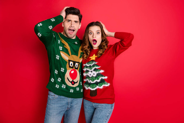 Portrait of impressed hipster couple hear unbelievable news scream wow omg wear deer christmas tree pattern jumper denim jeans isolated over red color background - Fotoğraf, Görsel