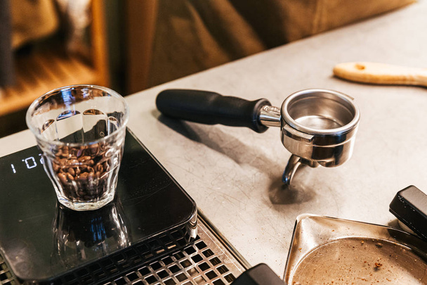 Kahve tezgahında boş kahve öğütücü grup kolu ile ağırlık ölçeğinde shot cam içinde Kahve çekirdekleri. - Fotoğraf, Görsel