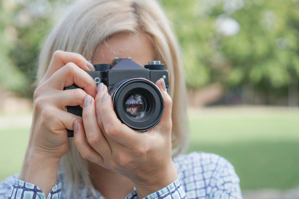 Girl blonde with a camera focuses in the park - Фото, зображення