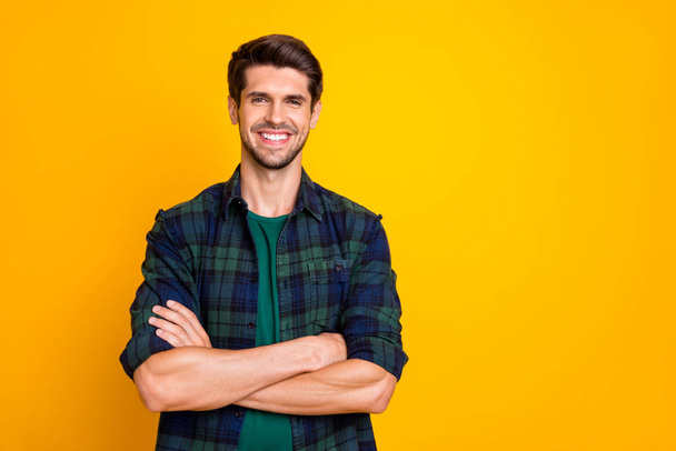 Photo of amazing macho guy with crossed hands toothy smiling glad to have good job wear casual plaid shirt isolated yellow color background - Fotoğraf, Görsel