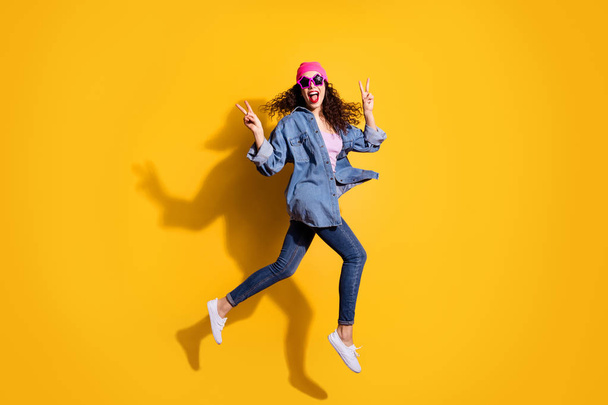 Full length photo of funky curly lady jumping high going to party showing v-sign symbols wear casual trendy clothes isolated yellow color background - Fotografie, Obrázek