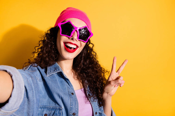 Photo of funny lady at disco party making selfies showing v-sign wear casual trendy clothes and cool star specs isolated yellow color background - Фото, зображення