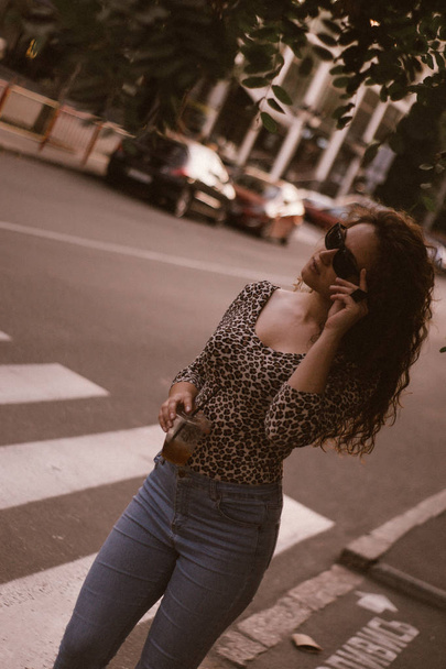 Happy curly young woman smiling outdoors and walking on city street at sunset time  - Foto, afbeelding