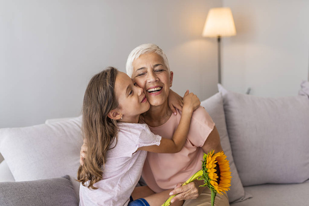 Happy grandmother hugging small cute grandchild thanking for flowers presented, excited granny embrace granddaughter congratulating her with birthday, making surprise presenting bouquet - Fotoğraf, Görsel