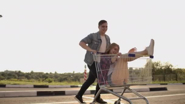 Człowiek biegnie i popycha wózek supermarket toczenia dziewczynę w nim, szalona zabawa studentów. - Materiał filmowy, wideo