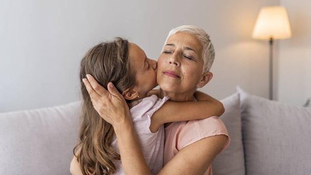 Granddaughter embracing her grandmother in living room. Her granddaughter holds the key to her heart. Grandmother and granddaughter. Smiling senior woman and girl embracing - Фото, зображення