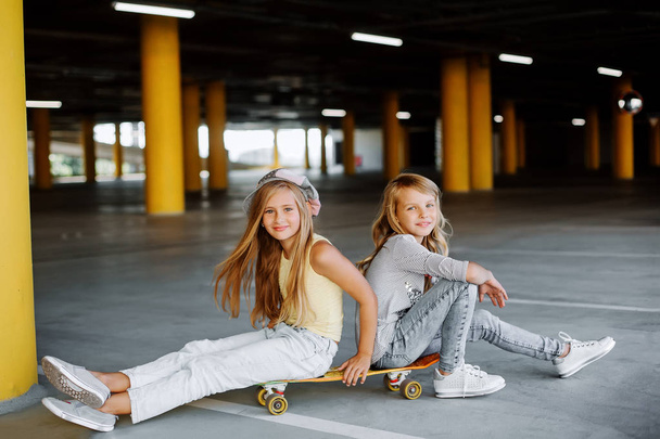 zwei schöne Mädchen Skateboard fahren, Spaß haben und auf dem Parkplatz spielen. Straßenfotoshooting - Foto, Bild