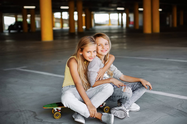 Dwie piękne dziewczyny skateboarding, zabawy i gry na parkingu. Ulica sesja zdjęciowa - Zdjęcie, obraz
