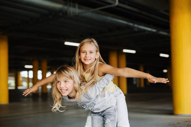 Two beautiful girls skateboarding, having fun and playing in the parking lot. Street photo shoot - Фото, изображение