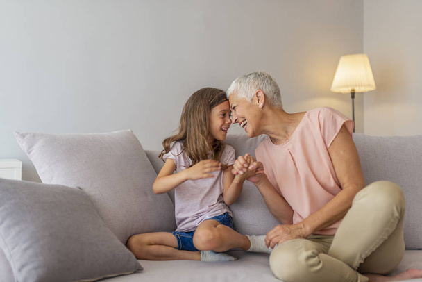 Happy middle-aged mature grandma and little preschool granddaughter touching noses laughing together, smiling loving old grandmother granny and cute carefree grandkid girl having fun playing at home - Фото, изображение