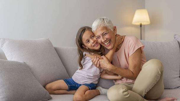 Happy senior woman hugging her beautiful grandchild at home. Portrait of grandmother and granddaughter. "My gran means the world to me". Little girl with grandmother - Zdjęcie, obraz