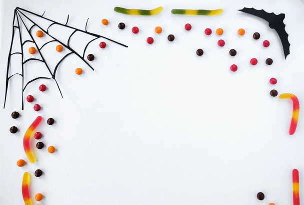 Хэллоуин украшения рамка с битой, паутиной, конфеты, сладкие черви на белом фоне. Кошелек или жизнь. Счастливый Хэллоуин. Принято. Вид сверху
 - Фото, изображение